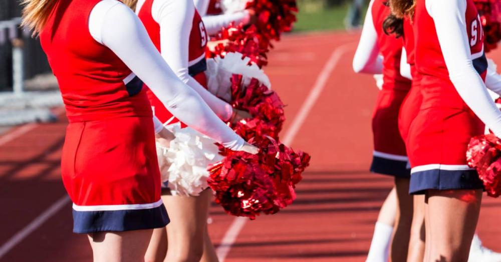 A group of cheerleaders dressed in black and red outfits. They are holding pompoms on the track field.