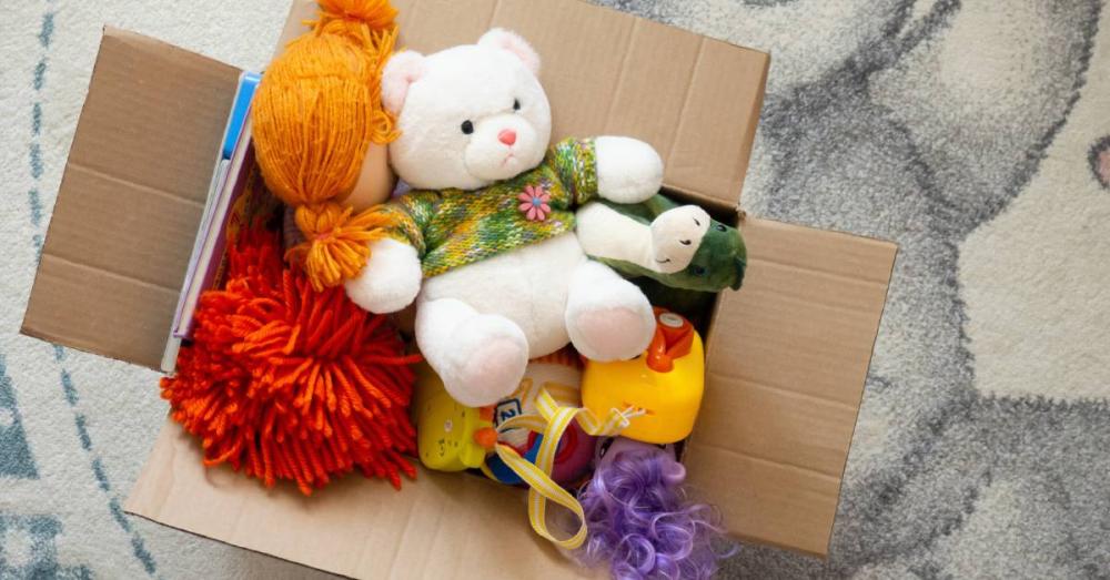 A cardboard box full of children’s toys. The box is overflowing with stuffed animals, dolls, and plastic toys.