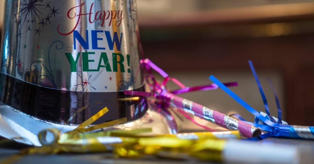 A decorative brim hat with text that says, “Happy New Year!” There are confetti party horns next to the hat.