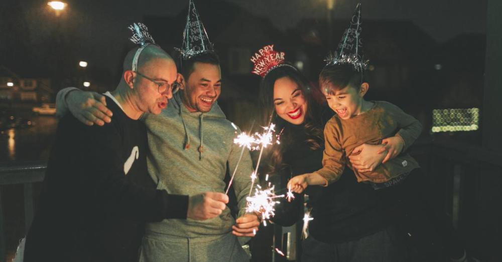 A family carefully holding ignited sparklers in their hands. They are wearing New Year’s Eve hats and headbands.