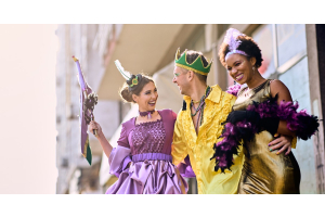 Three Mardi Gras participants are dressed in traditional Mardi Gras colors. They have eccentric makeup and accessories.