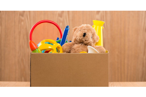 A cardboard box filled with children’s toys. There are plastic toys and a teddy bear sticking out from the top.