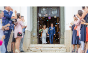 Newlyweds leaving a chapel holding hands. Wedding attendees stand to create an aisle for the newlyweds to walk through.