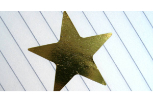 Lined paper with a gold star sticker. There is written text that says “well done!” next to the sticker.