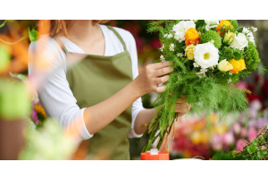 A woman arranging a bouquet in a floral shop. The bouquet consists of yellow, white, and green flowers.