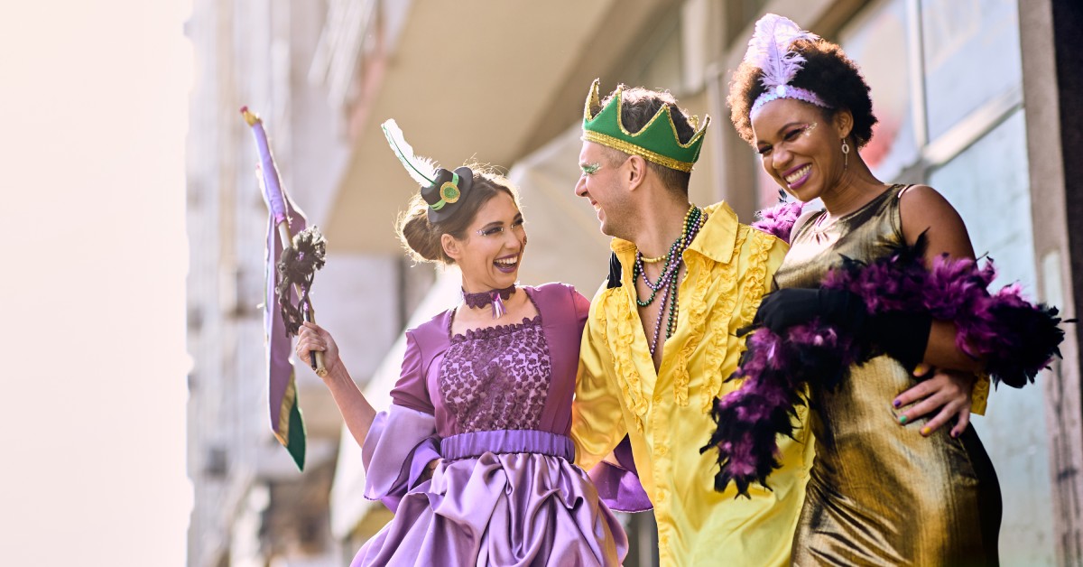 Three Mardi Gras participants are dressed in traditional Mardi Gras colors. They have eccentric makeup and accessories.