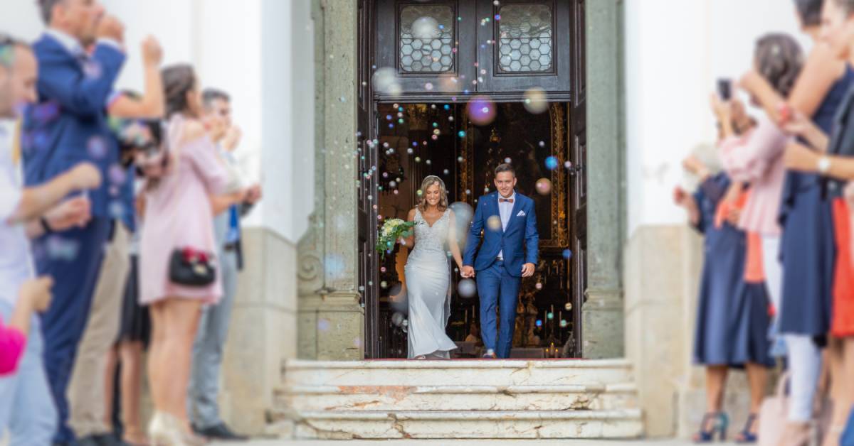 Newlyweds leaving a chapel holding hands. Wedding attendees stand to create an aisle for the newlyweds to walk through.