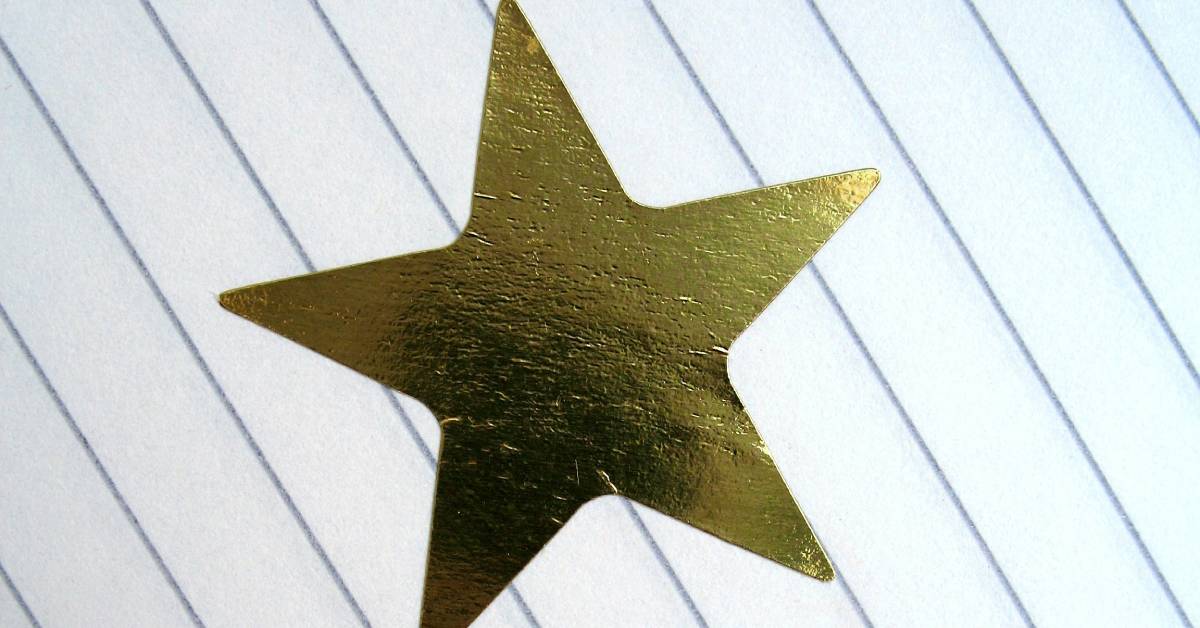 Lined paper with a gold star sticker. There is written text that says “well done!” next to the sticker.