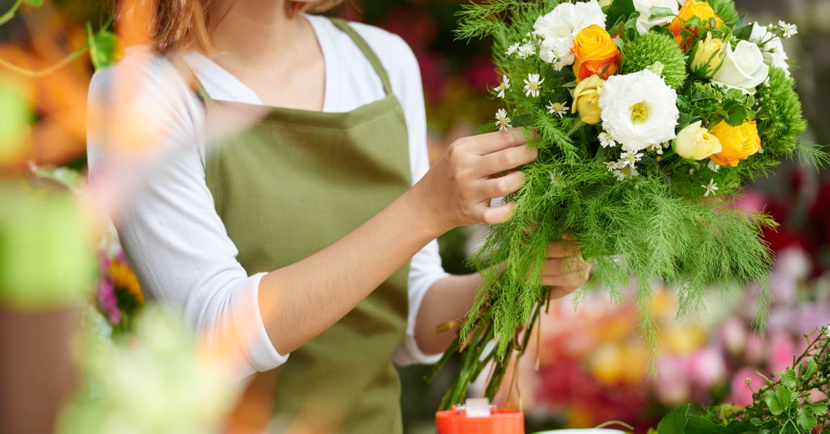 A woman arranging a bouquet in a floral shop. The bouquet consists of yellow, white, and green flowers.