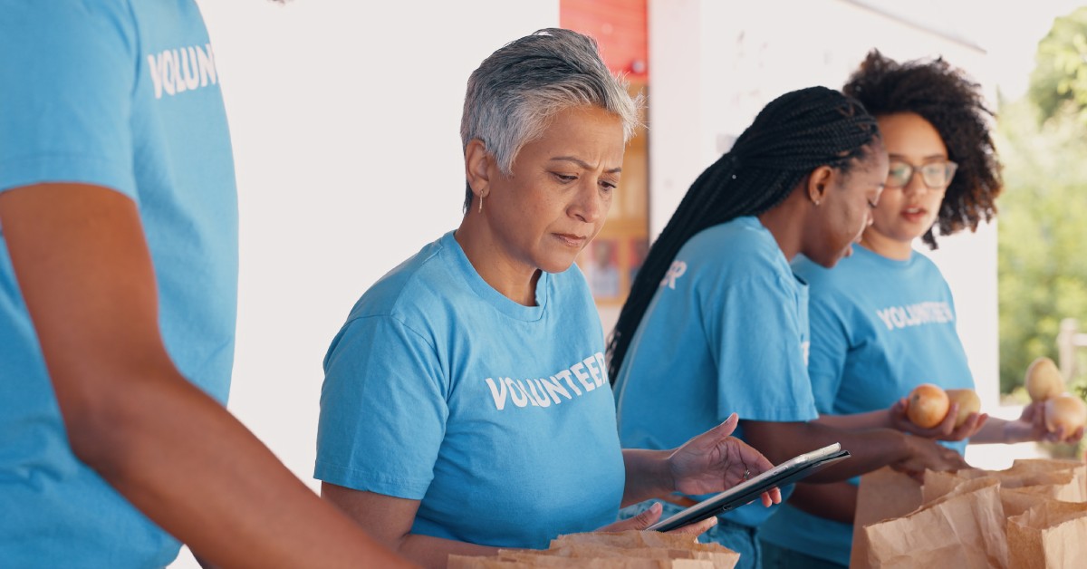 A group of volunteers organizing a food drive. They are sorting food and keeping track of inventory on a tablet.