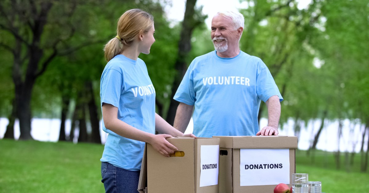 Two volunteers talking at a charity event. They are both holding brown boxes labeled “donations” on the side.