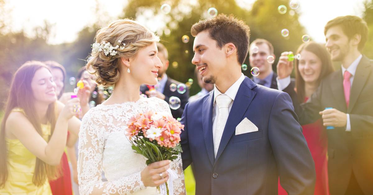 A wedding couple standing in the middle of their wedding guests. The guests are blowing bubbles in their direction.